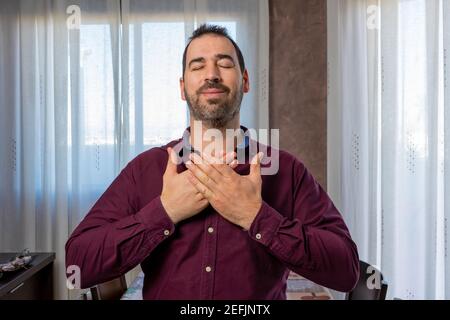 Homme barbu dans une chemise violette avec ses mains sur sa poitrine et ses yeux fermés. Concept de paix Banque D'Images