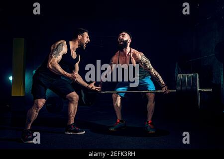 Deux barbus tattoed musculaire, l'entraînement des athlètes un ascenseur bar poids lourd lorsque d'autres est motivant. Scream. Travailler dur. Exercice pour les muscles du dos Banque D'Images