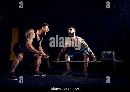 Deux barbus tattoed musculaire, l'entraînement des athlètes un ascenseur bar poids lourd lorsque d'autres est motivant. Scream. Travailler dur. Exercice pour les muscles du dos Banque D'Images