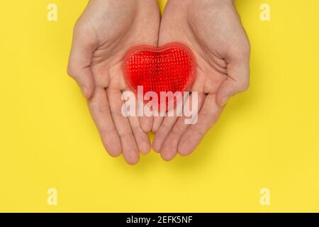 Les mains des hommes tiennent un coeur rouge sur un fond jaune. Amour, concept de relation. Symbole romantique, carte cadeau pour la Saint-Valentin Banque D'Images