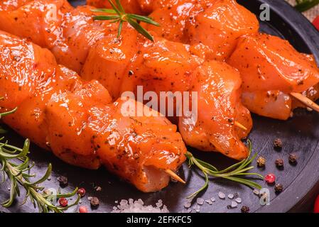 Morceaux de poulet de kebabs marinés dans une marinade rouge avec des épices sur un tableau culinaire sombre, sur un fond avec des morceaux de poivre. Morceaux de poulet crus Banque D'Images