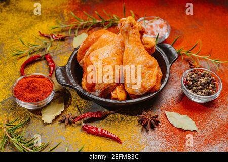 Pilons de poulet marinés crus parsemés d'épices, de piments, de feuilles de Laurier préparées pour cuire dans un plat, vue d'en haut Banque D'Images