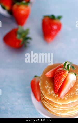 Crêpes américaines savoureuses avec fraises sur plaque blanche sur fond bleu. Banque D'Images