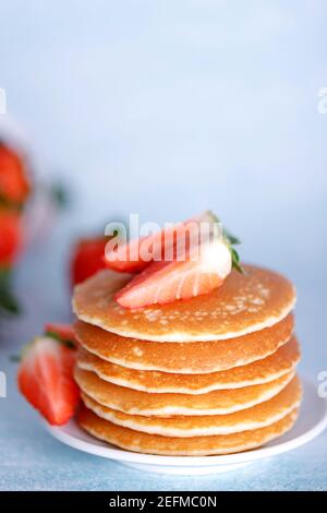 Crêpes américaines savoureuses avec fraises sur plaque blanche sur fond bleu. Banque D'Images