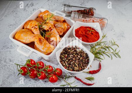 Pilons de poulet marinés crus parsemés d'épices, de piments, de feuilles de Laurier préparées pour cuire dans un plat, vue d'en haut Banque D'Images