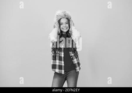 Ajouter un peu de personnalité pour temps froid armoire. Heureux l'enfant porter un chapeau en fausse fourrure. Petite fille sourire dans hat fond jaune. Chaud et moelleux pour trapper hat kid. Fashion hat pour des aventures en plein air. Banque D'Images