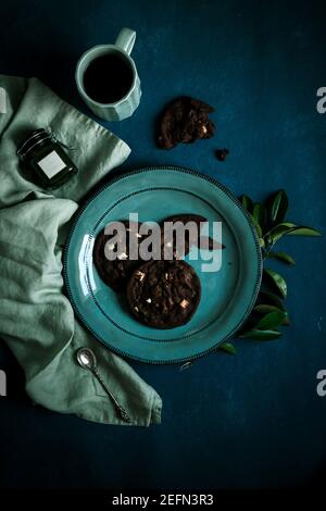 biscuits au chocolat avec une tasse de thé noir sur l'assiette turquoise avec une cuillère sur fond bleu. plat Banque D'Images