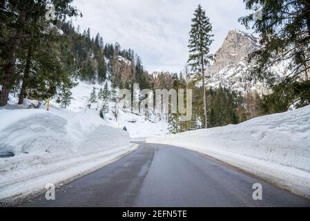 Route sinueuse de montagne déserte avec de la neige à refus sur les deux flancs dans un paysage de montagne boisé d'hiver sur un ciel nuageux jour Banque D'Images