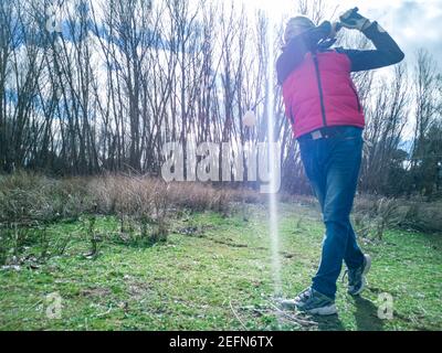 Senior citoyen pratiquant son swing de golf sur un terrain rustique par temps nuageux Banque D'Images