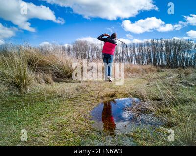 Senior citoyen pratiquant son swing de golf sur un terrain rustique par temps nuageux Banque D'Images