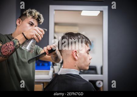 le coiffeur lance les cheveux du client avec un spray, puis les peignes. Banque D'Images