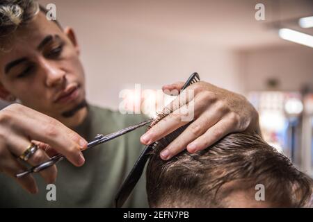 portrait d'un coiffeur qui coupe les cheveux de son client avec ciseaux Banque D'Images