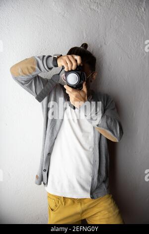 Un jeune photographe élégant, habillé à la mode, prend une photo. Il a un fond blanc derrière lui. Concept de photographe Banque D'Images