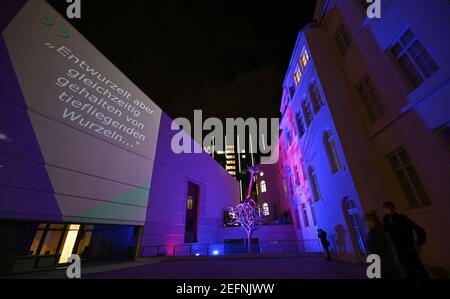 17 février 2021, Hessen, Francfort-sur-le-main: Alors que les mots «déracinés mais en même temps détenus par des racines profondes.» sont projetés sur la façade du Musée juif, la sculpture d'arbre sur la piste est baignée de lumière colorée. Le Musée juif de Francfort présentera une installation interactive de lumière et de son sur sa piste à partir du 18 février. Les projections peuvent être vues quotidiennement entre 7 et 10 heures autour de la sculpture créée spécialement pour la place, intitulée 'United', qui se compose de deux arbres en fonte d'aluminium, dont l'un atteint dans le ciel avec ses racines. Photo: Arne D. Banque D'Images