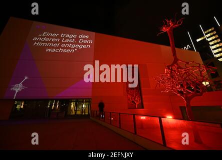 17 février 2021, Hessen, Francfort-sur-le-main: Alors que les mots «l'un porte le fardeau de l'autre. Poussant vers le ciel sont projetées sur la façade du Musée juif, la sculpture d'arbre sur la piste est baignée de lumière rouge. Le Musée juif de Francfort présentera une installation interactive de lumière et de son sur sa piste à partir du 18 février. Les projections peuvent être vues quotidiennement entre 7 et 10 heures autour de la sculpture créée spécialement pour la place, intitulée 'United', qui se compose de deux arbres en fonte d'aluminium, dont l'un atteint dans le ciel avec ses racines. Photo: Arne Dedert/dpa Banque D'Images