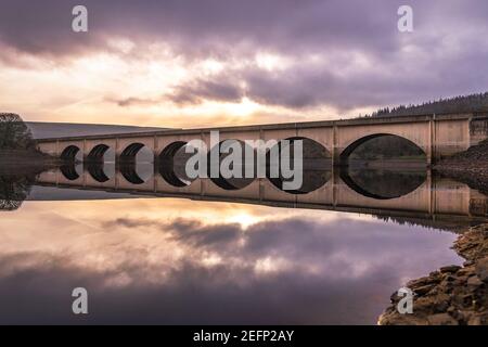 Long pont voûté traversant le réservoir de Ladybower se reflétant dans la vallée de Derwent eau de rivière encore profonde avec lever de soleil magnifique cadre de ciel orange derrière Banque D'Images