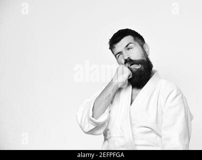 Homme de karaté avec le visage de souffrance en uniforme. Concept des arts martiaux japonais. Homme avec barbe dans un kimono blanc sur fond blanc. Le maître de Judo se frappe avec la poing Banque D'Images