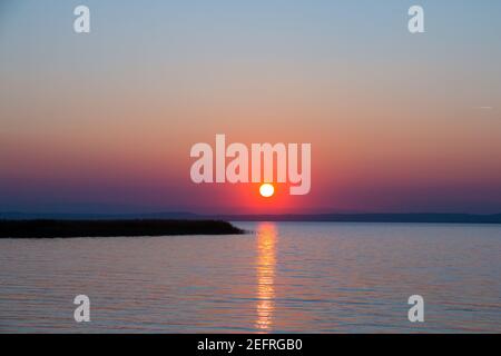 Soleil doré sur la mer juste au-dessus de l'horizon avec une ligne optique droite de réflexion de lumière sur la surface de l'eau, magnifique paysage naturel de coucher de soleil avec Banque D'Images