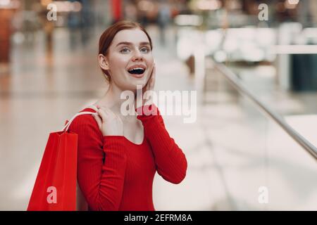 Jeune femme avec des sacs rouges en papier dans le centre commercial. Concept du Vendredi fou et de la Saint-Valentin. Banque D'Images