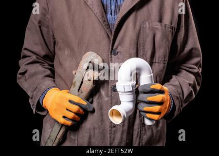 Plombier tenant une clé réglable et un siphon dans le lavabo. Ouvrier répare le circuit hydraulique. Arrière-plan sombre. Banque D'Images