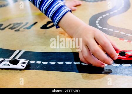 Enfant joue avec deux voitures miniatures dans un jouet circuit. Banque D'Images