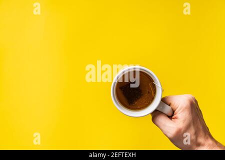 Vue de dessus des mains tenant une tasse de thé devant de fond jaune Banque D'Images