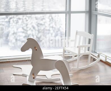 Un coin enfants lumineux et confortable de la maison avec un Fauteuil à bascule et cheval de style scandinave le fond d'une grande fenêtre en hiver Banque D'Images