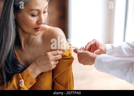 Vaccination et prévention de COVID19. Les mains des femmes du médecin ou de l'infirmière administrant l'injection du vaccin à un patient mature à cheveux gris à l'hôpital. Injection de remède de coronavirus dans la femme d'âge moyen Banque D'Images