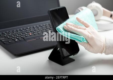 Femme en gants utilise un spray antiseptique pour nettoyer l'espace de travail de smartphomeon. Désinfection du phomeand ordinateur portable clavier par alcool désinfectant par femme en lueur Banque D'Images