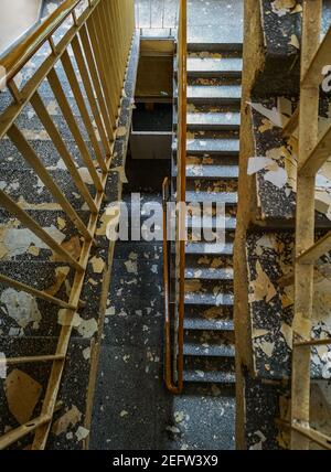 Vue de dessus en bas de l'escalier en béton avec des rails en métal et peintures décortiquées des murs de l'ancien hôpital abandonné Banque D'Images