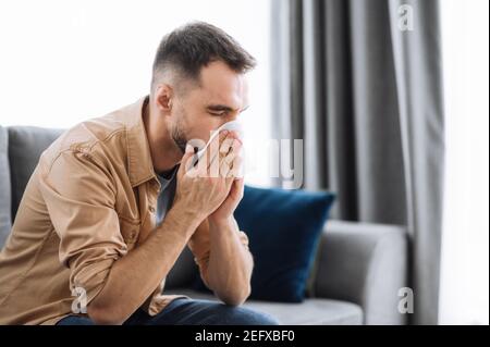 Malade caucasien gars assis sur le canapé se sentent malsains, il souffrant de rhinite se tarra, ayant une infection respiratoire, obtenir la fumée, assis à la maison à la quarantaine Banque D'Images