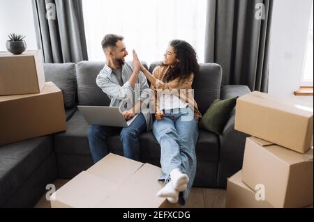 Un couple heureux et marié déménagera dans un nouvel appartement. Une jeune famille pleine de joie approuve le design de la maison intérieure, faisant de bons achats en ligne. Beau homme donner haut cinq à belle femme, concept de travail d'équipe Banque D'Images