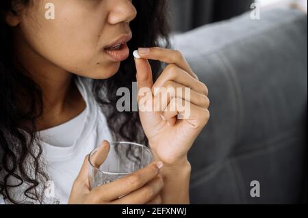 Gros plan photo d'une jeune femme afro-américaine, prendre une pilule à cause de se sentir mal. La femme malsaine souffre de stress, de maladie ou de grippe. Concept de maladie Banque D'Images