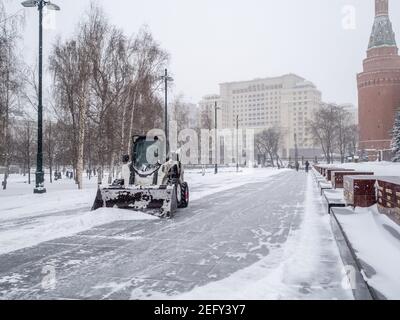 Moscou. Russie. 12 février 2021. Un petit bobcat de pelle-chargeuse enlève la neige du trottoir près des murs du Kremlin lors d'une forte chute de neige Banque D'Images