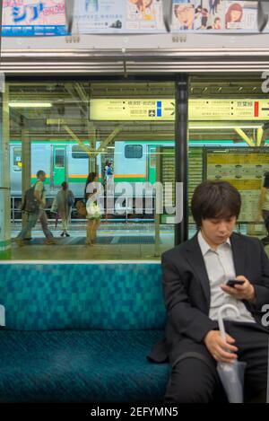 Un homme regarde son téléphone mobile en attendant dans le métro de Tokyo, au Japon Banque D'Images