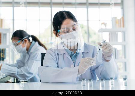 Belle jeune scientifique féminine portant un masque facial et un écran de performance recherche médicale en laboratoire hospitalier avec un collègue Banque D'Images