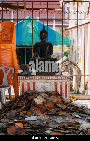 Statue de bouddha noir assise derrière une pile de tuiles de toit dans le temple en cours de rénovation. Banque D'Images