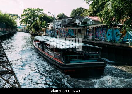 Le bateau de transport Khlong traverse un canal sale à Bangkok en Thaïlande, avec des graffitis sur le côté. Banque D'Images