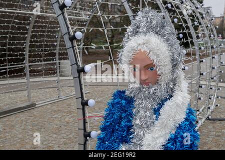 Mannequin de neige garnie d'un manteau de fourrure bleu avec frange blanche debout sur une plate-forme bordée de pierres près d'une arche métallique avec rangées de lampes éclairantes. Banque D'Images