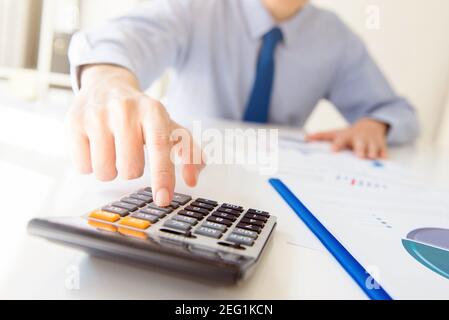 Homme d'affaires appuyant sur le bouton de la calculatrice à la table de travail dans le bureau - concept d'analyse financière Banque D'Images