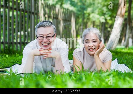 Bon vieux couple assis sur l'herbe du parc à regarder la caméra Banque D'Images