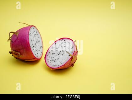 Deux moitiés de fruit dragon à chair blanche sur fond jaune. Le fruit de pitaya à la peau rose est pauvre en calories, rempli de vitamines essentielles et de M. Banque D'Images