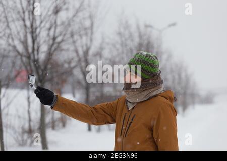 L'homme photographie par le petit appareil photo dans la neige profonde. Nature, tempête dans le parc urbain. Activités de plein air. Banque D'Images