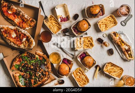 Verrouillez le concept de restauration rapide du service de livraison. Plat de quarantaine de la fête maison avec hamburgers, frites, sandwichs, pizza, bière dans des verres sur fond blanc de nappe, vue du dessus Banque D'Images