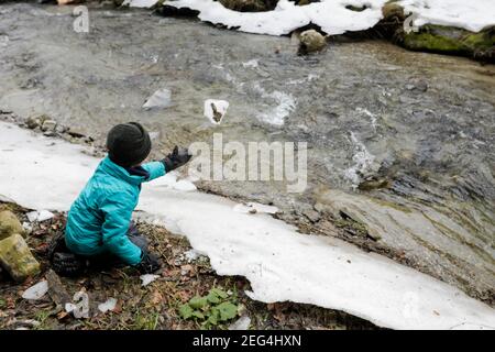 Jeune garçon jouant près d'un ruisseau de montagne pendant une journée d'hiver enneigée dans les montagnes roumaines des Carpates. Banque D'Images