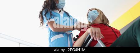 Kinésithérapeute effectuant un massage du dos et de l'épaule à une jeune femme handicapée en fauteuil roulant portant des masques médicaux de protection Banque D'Images