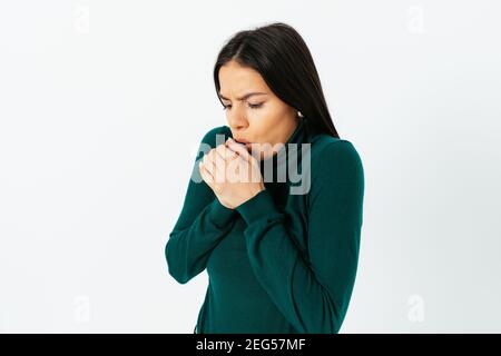 Une jeune femme verglaçante portant un pull à col roulé vert souffle sur ses mains en essayant de rester au chaud. Banque D'Images