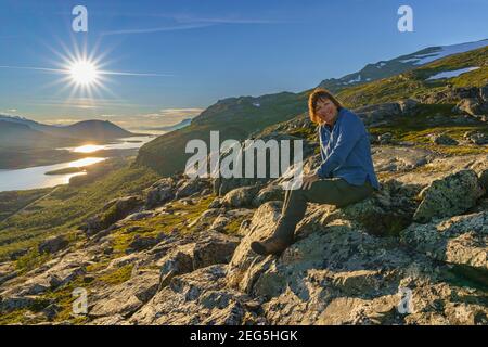 Femme assise sur une montagne bénéficiant de la vue par beau soleil, stora sjöfallet nationalpark, Laponie suédoise, Suède Banque D'Images