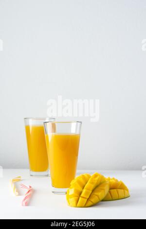 Jus de mangue dans des verres avec du jus et une paille sur fond blanc, mangue hachée et toute, délicieuse boisson naturelle douce et saine Banque D'Images