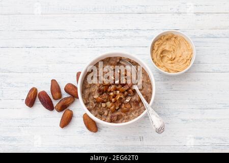 Délicieux flocons d'avoine dans un bol blanc, dattes fruits, cacao et beurre d'arachide. Petit déjeuner sain sur fond bleu clair. Espace libre. Vue sur le dessus Banque D'Images